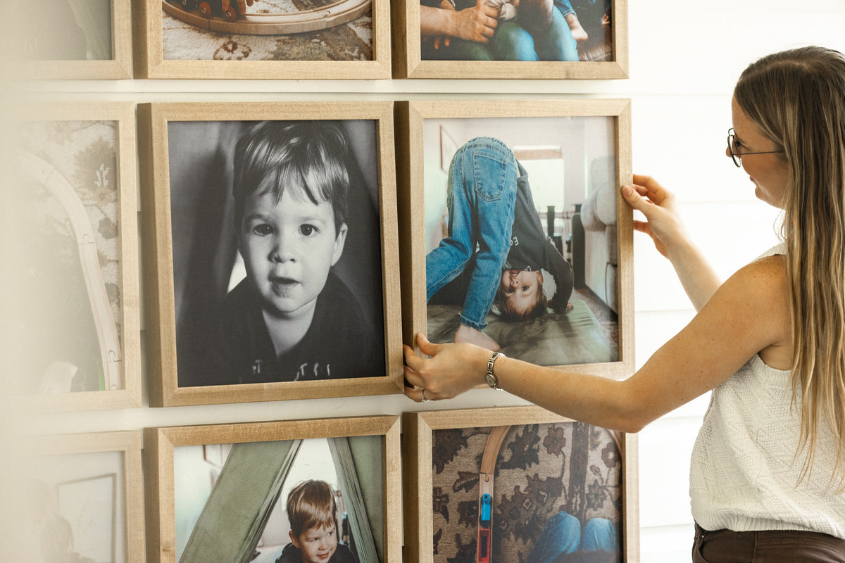 A woman straightening a set of square framed photos