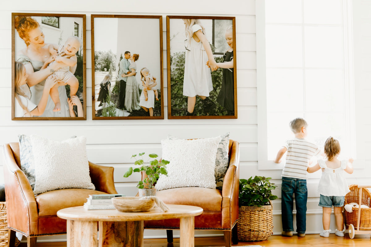 Three framed family photos above chairs while two kids look out the window