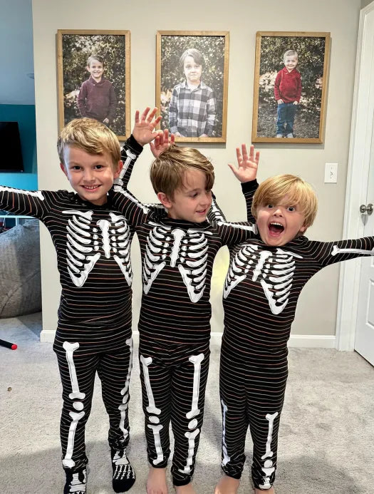 Three brothers in skeleton pajamas under their framed portraits